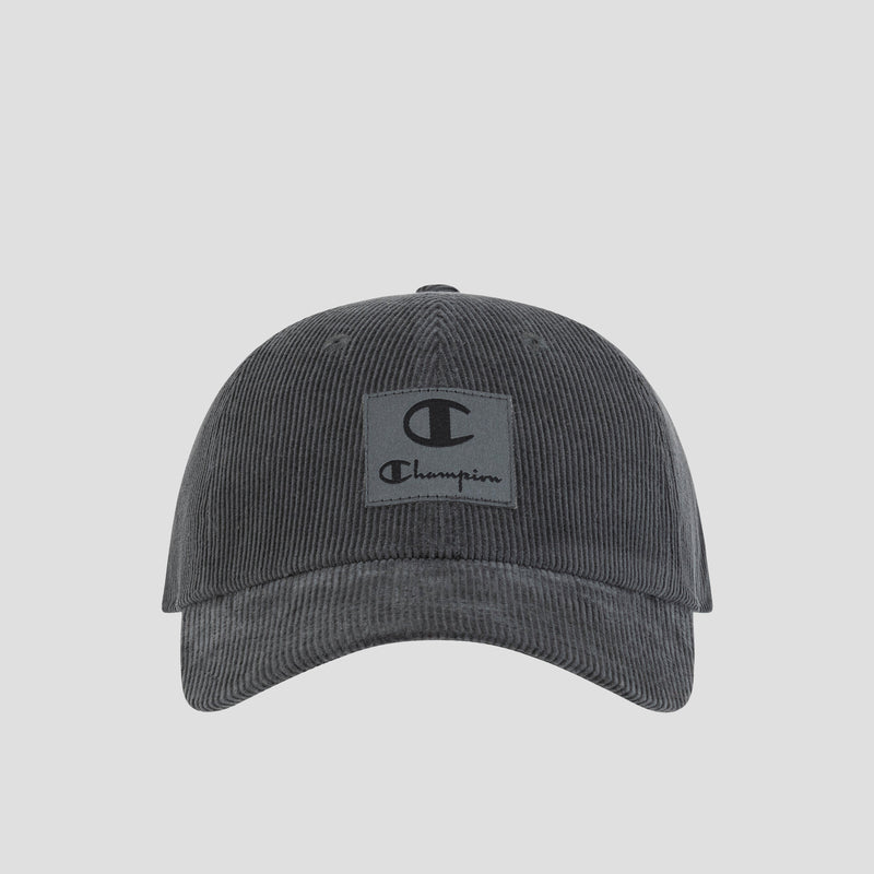Introducing the Ridge Corduroy Adjustable Cap by Champion—a dark grey vintage-inspired baseball cap crafted from corduroy. Featuring a relaxed fit, curved brim, and an adjustable back closure for custom comfort, this cap showcases a rectangular front patch with the iconic Champion logo and text. Photographed on a plain white background.