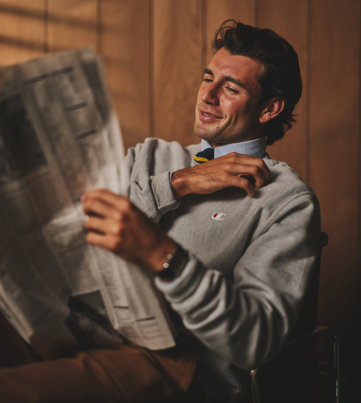 Man reading a newspaper with a bow tie and Champion sweatshirt.