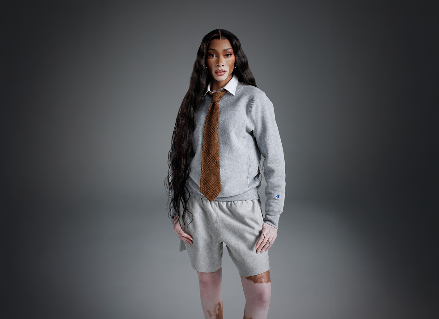 Woman wearing a gray outfit with a patterned tie against a gray background