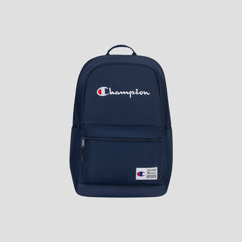 Introducing the Champion System Backpack in navy blue, designed with multiple storage compartments—including a front zipper pocket, side pocket, and a padded laptop sleeve for added convenience. The backpack showcases the distinctive white and red Champion logo on the front, set against a light grey background in the photograph.