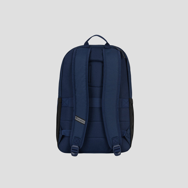 The System Backpack by Champion is displayed from the back against a plain light gray background, showcasing its navy blue color, padded shoulder straps, top carry handle, and multiple storage compartments—including a padded laptop sleeve.