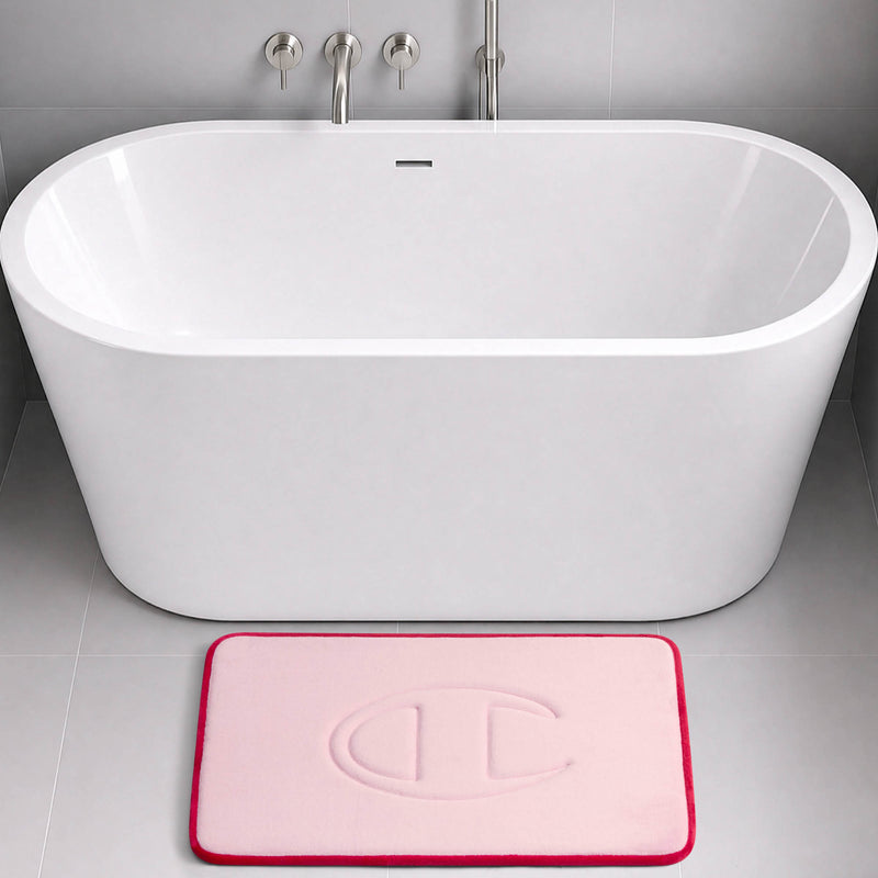 A modern white bathtub with a light pink Champion Quilted Logo Memory Foam Bath Mat, featuring an embossed circular design, placed on a light gray tiled bathroom floor.