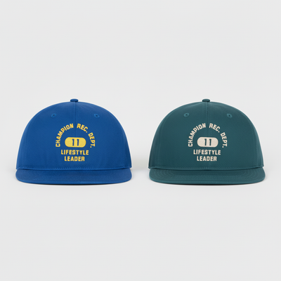 The Champion Athletic Dept Flat Brim Cap 2 Pack includes a blue and a dark green cap, each with "CHAMPION REC. DEPT. LIFESTYLE LEADER" text and a yellow-and-white "1" emblem on the front.