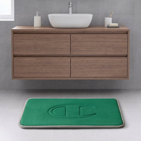 Modern bathroom with a floating wood vanity, white vessel sink, and a Champion Quilted Logo Memory Foam Bath Mat featuring a large embossed letter C on a light gray tiled floor.