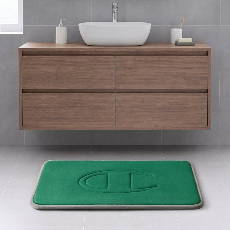 Modern bathroom with a floating wood vanity, white vessel sink, and a Champion Quilted Logo Memory Foam Bath Mat featuring a large embossed letter C on a light gray tiled floor.