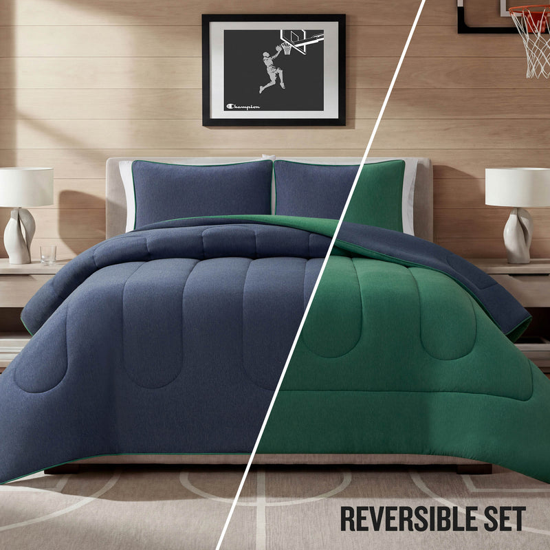 A neatly made bed features the Champion Premium Reversible Solid Jersey Comforter Set in blue and green, matching pillows, two bedside tables with lamps, and a framed basketball artwork above the headboard. The text “REVERSIBLE SET” appears at the bottom right.