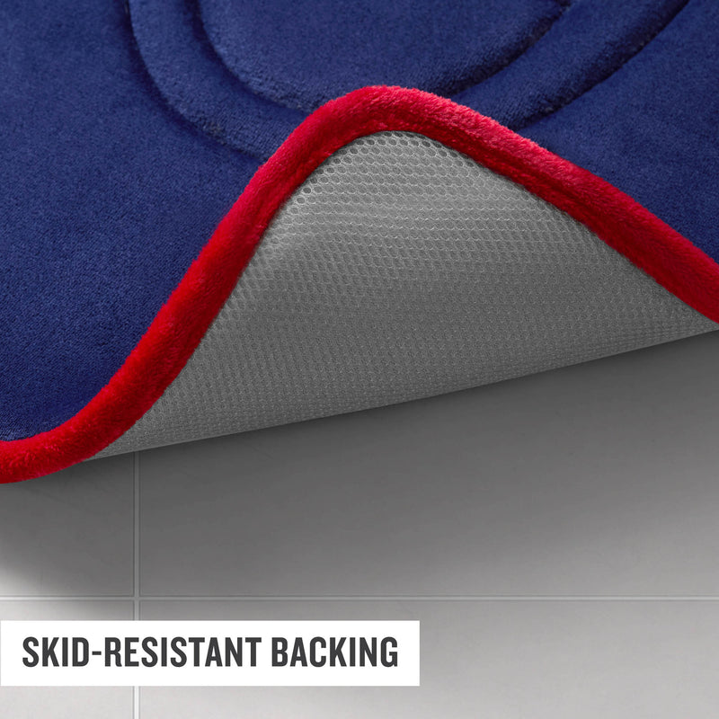 A close-up of a blue Champion Quilted Logo Memory Foam Bath Mat with a red edge, partially lifted to reveal its white, textured skid-resistant backing on a tiled floor. Text reads SKID-RESISTANT BACKING.