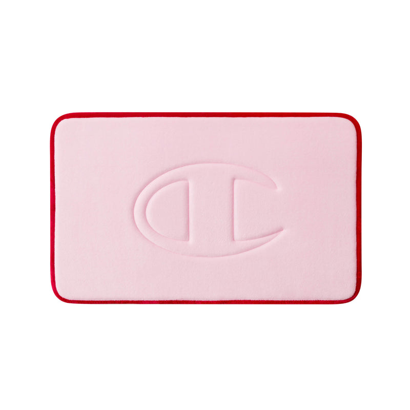 A rectangular pink Champion Quilted Logo Memory Foam Bath Mat with rounded corners and a red border, featuring an embossed large C-shaped logo in the center.