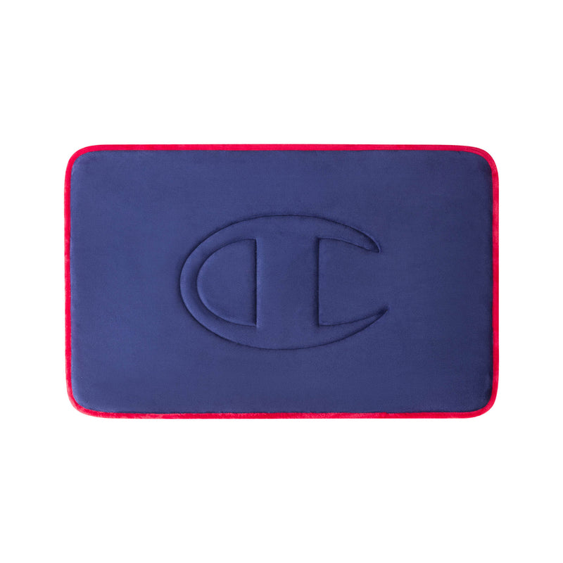 A rectangular navy blue Quilted Logo Memory Foam Bath Mat by Champion, featuring rounded corners, red edges, and an embossed large C logo in the center, displayed against a white background.