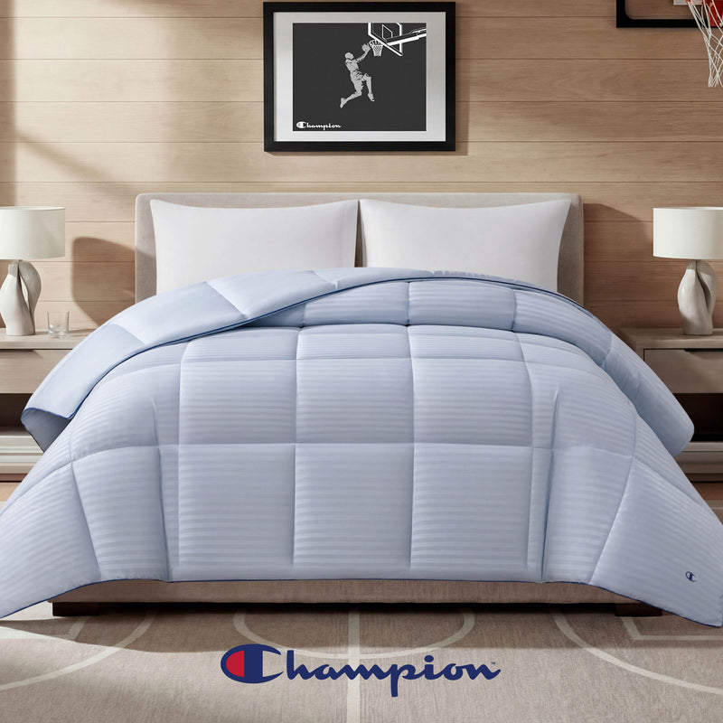 A neatly made bed showcases the Champion Blue Cooling Down Alternative Comforter, complemented by two pillows, nightstands with lamps, and a distinctive Champion logo at the foot of the bed. Basketball-themed framed art hangs on the wall behind, completing this stylish setup featuring Champion bedding.