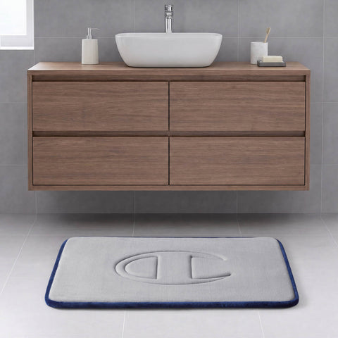 A modern bathroom with a floating wooden vanity, a vessel sink, and a rectangular gray Quilted Logo Memory Foam Bath Mat from Champion, featuring an embossed logo, set on a light tile floor.