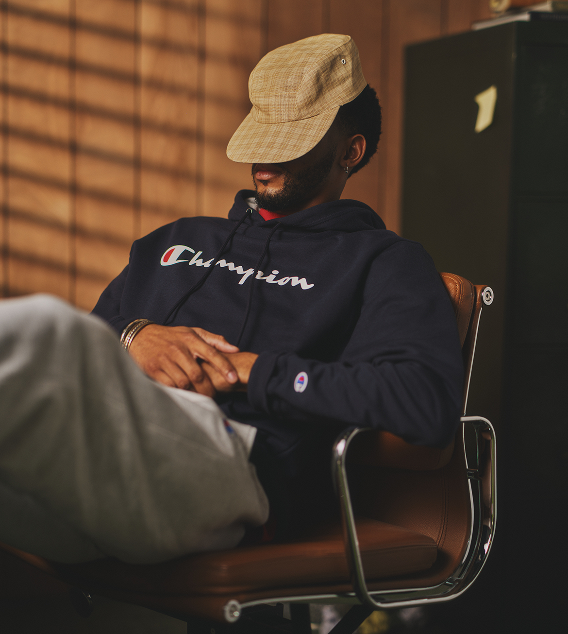 Person wearing a Champion hoodie and cap sitting on a chair.