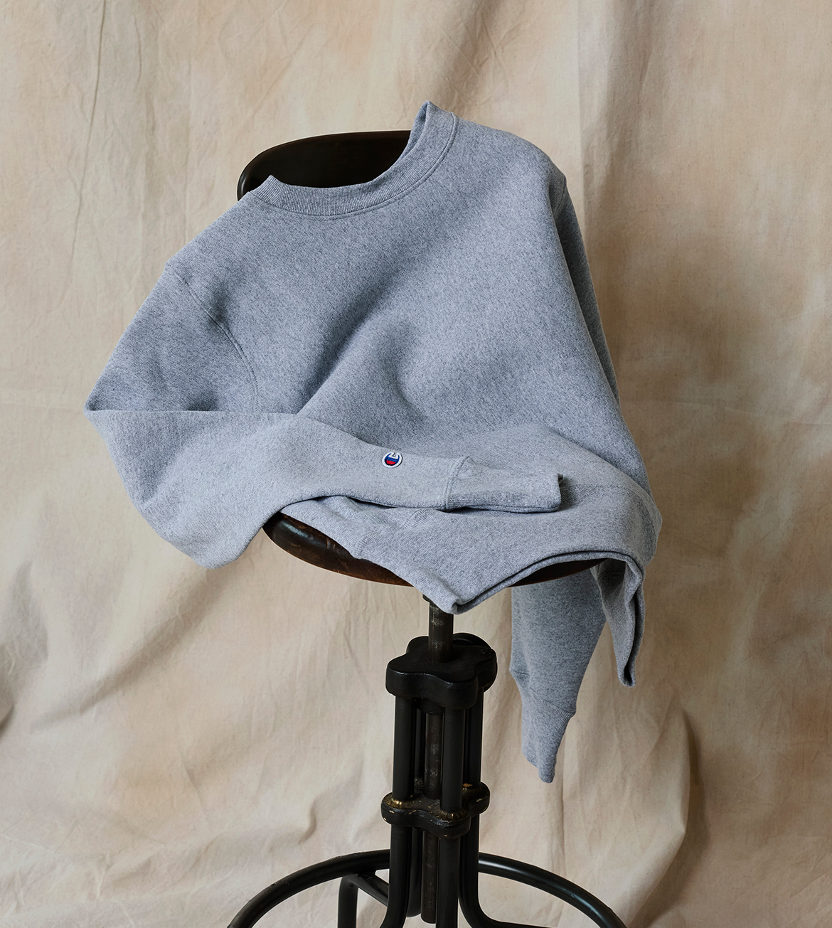 Gray sweatshirt on a black stool against a beige curtain background