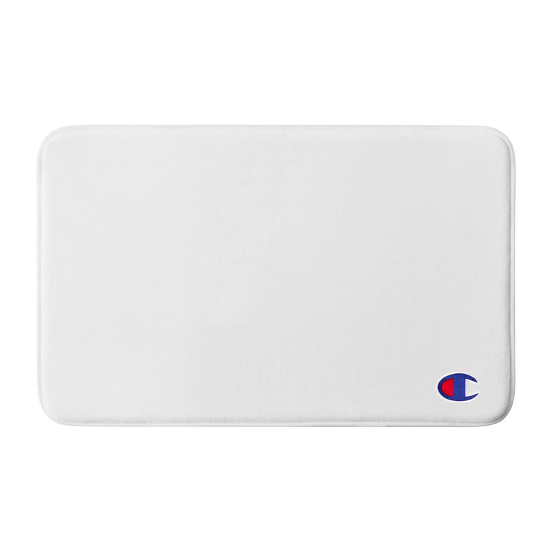 A plain white rectangular Champion Logo Patch Memory Foam Bath Mat with rounded corners and a small blue and red Champion logo in the bottom right corner. This skid-resistant bath mat offers both comfort and safety for your bathroom.