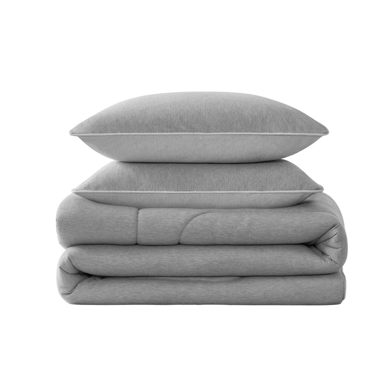 Two gray pillows are stacked on top of a neatly folded Champion Premium Reversible Solid Jersey Comforter Set, all set against a plain white background.