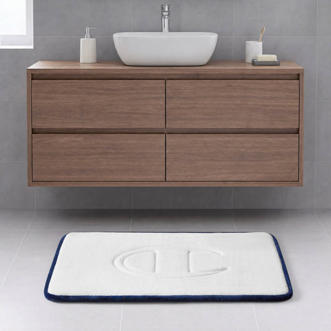 A modern bathroom with a floating wooden vanity, a vessel sink, a soap dish, and the Champion Quilted Logo Memory Foam Bath Mat—with plush cushioning and an embossed logo—accents the light gray tiled floor with its white surface bordered in blue.