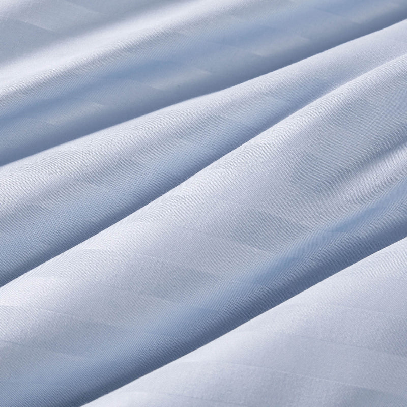 Close-up of smooth, light blue fabric with gentle diagonal folds and a subtle, horizontal striped texture. The material appears soft and slightly shiny, reminiscent of the fabric used in the Champion Blue Cooling Down Alternative Comforter.