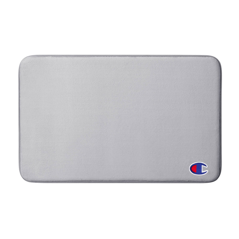 A rectangular light gray Champion Logo Patch Memory Foam Bath Mat features rounded corners and a small red, white, and blue Champion logo in the bottom right corner. This skid-resistant bath mat offers both comfort and style, making it a perfect addition to any bathroom.