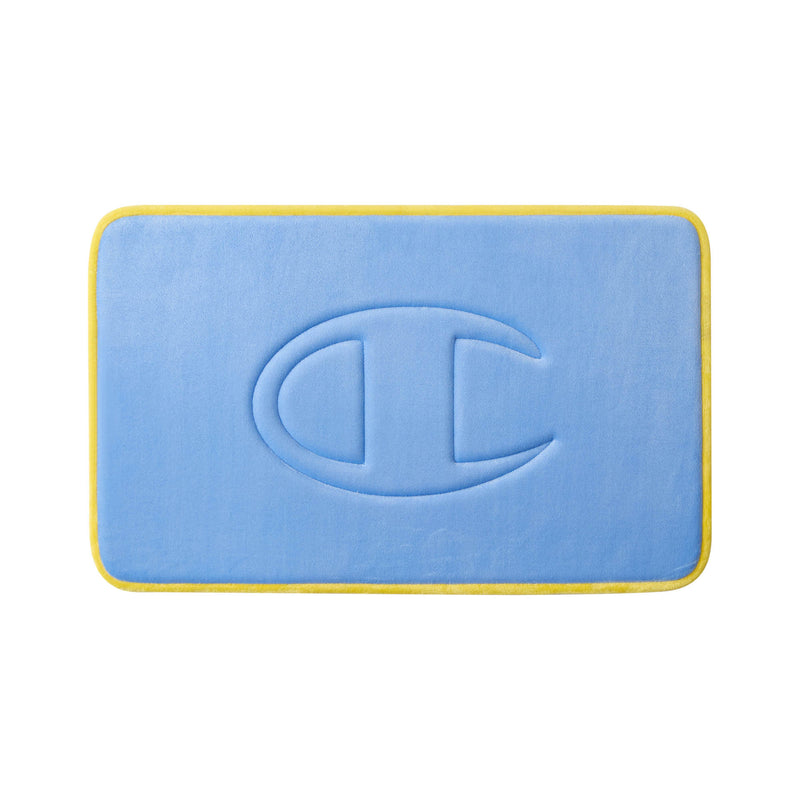 A rectangular blue Quilted Logo Memory Foam Bath Mat by Champion features rounded corners, yellow trim, and an embossed large C shape design in the center. This stylish bath mat is photographed on a white background.
