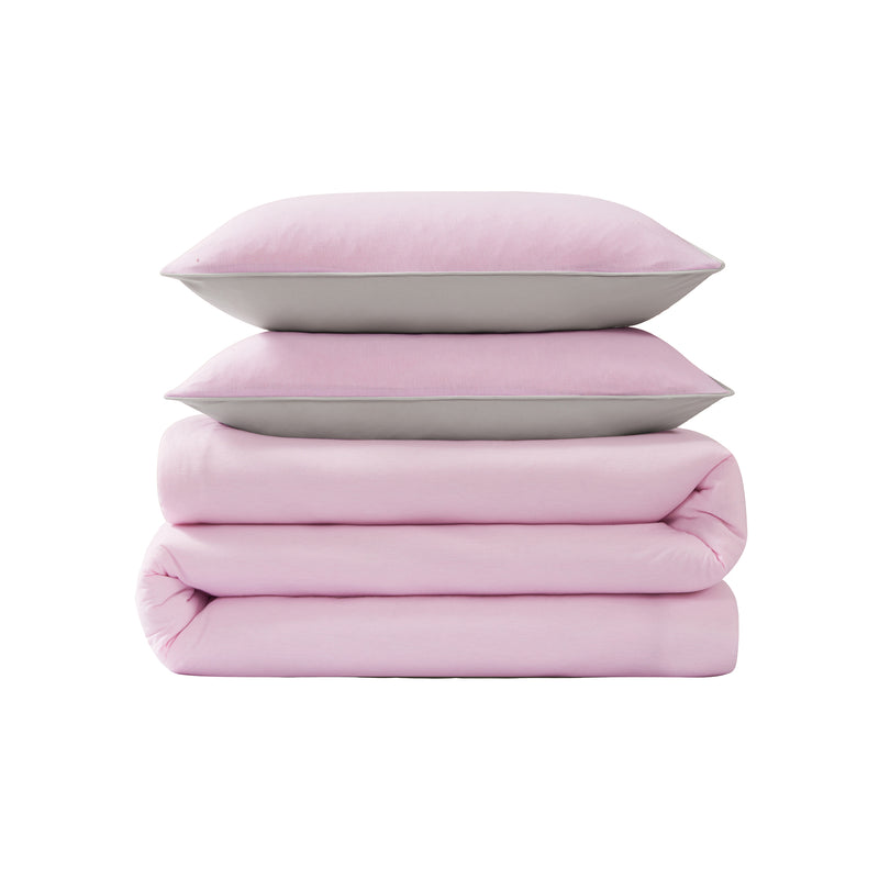 Two pillows and two folded blankets, all in soft pastel pink, are stacked neatly on top of each other against a plain white background, capturing the cozy appeal of Champion’s Reversible Solid Jersey Comforter Sets—perfect for those who appreciate athletic-inspired bedding with both style and comfort.