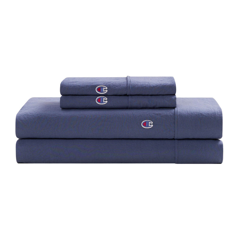 A neatly folded Champion Embroidery Patch Microfiber Sheet Set in dark blue, including bed sheets and pillowcases crafted from soft microfiber fabric, each adorned with a small embroidered Champion logo, stacked on a white background.