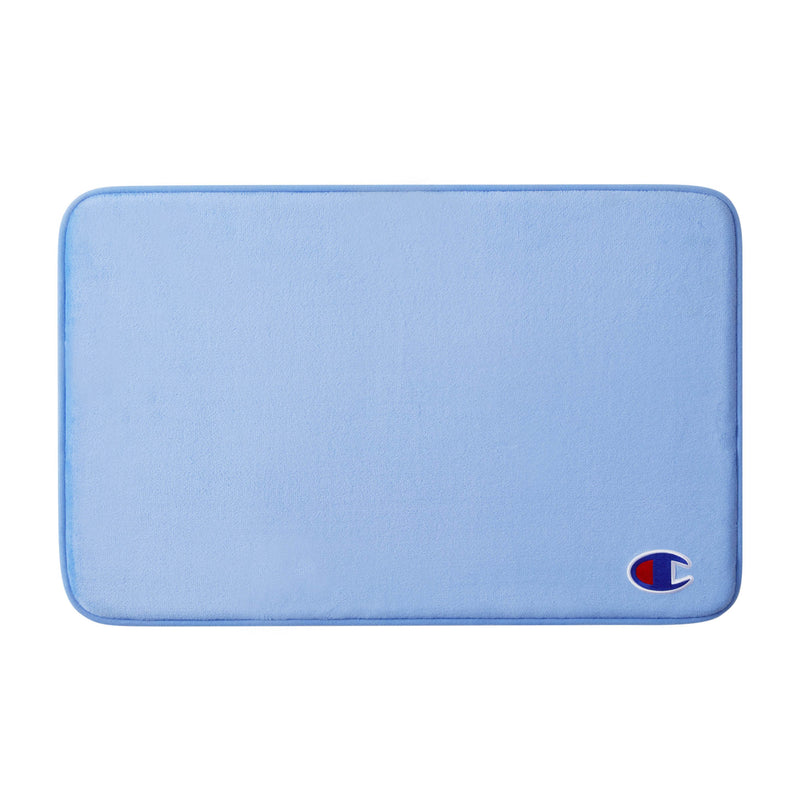 The Champion Logo Patch Memory Foam Bath Mat is a rectangular, light blue mat with rounded corners and a small Champion logo patch in the bottom right corner. It features a skid-resistant backing for added safety and comfort.