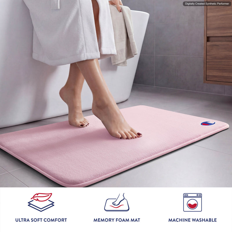 A person steps out of a bathtub onto a pink Champion Logo Patch Memory Foam Bath Mat. This skid-resistant mat showcases the Champion embroidered logo patch in one corner. Icons below highlight its ultra-soft comfort, memory foam cushioning, and machine washable convenience.