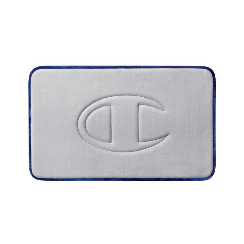 A light gray, rectangular Quilted Logo Memory Foam Bath Mat by Champion features rounded corners, dark blue edging, and a large embossed Champion “C” logo at the center. This stylish bath mat provides both comfort and a modern touch to your bathroom space.