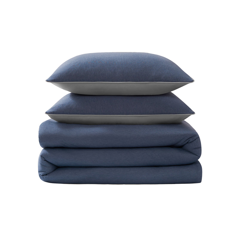 A neatly folded Champion Reversible Solid Jersey Comforter Set in blue, with two matching blue pillows stacked on top, set against a white background.