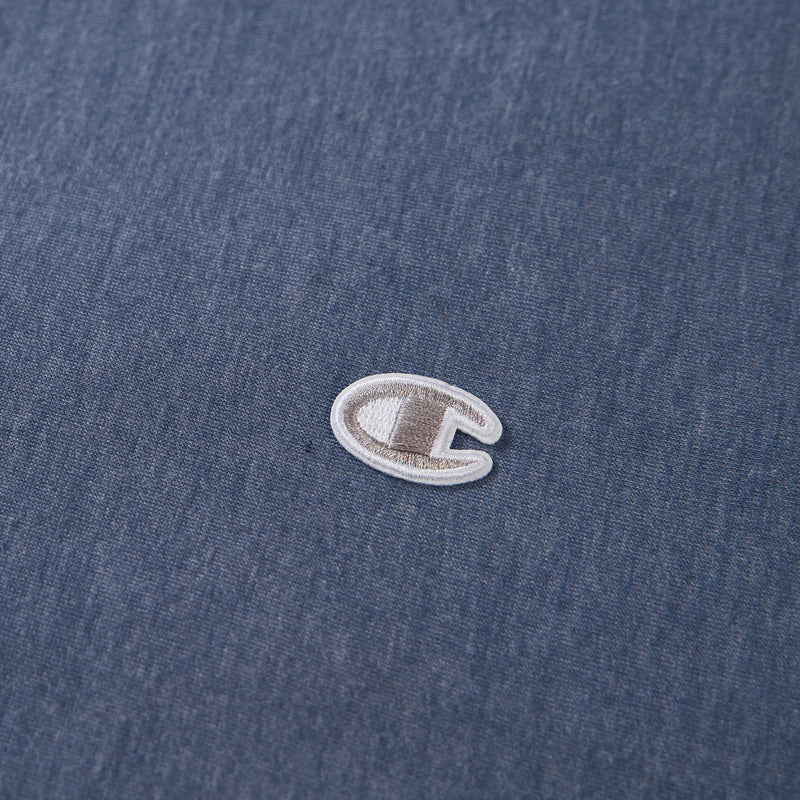 A close-up of a small embroidered Champion logo on blue fabric, featuring the distinctive white and gray C symbol centered on the material—an ideal accent for Champion’s Reversible Solid Jersey Comforter Sets or any athletic bedding collection.