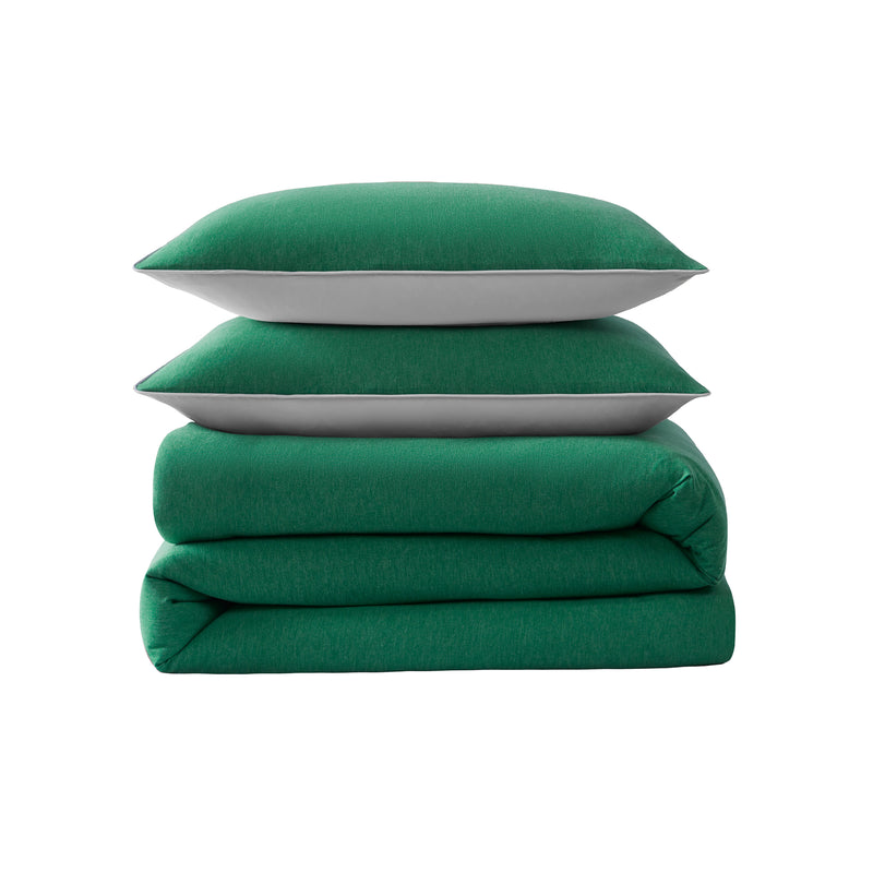 A set of two green pillows is stacked on top of a folded Champion Reversible Solid Jersey Comforter Set, with white backgrounds visible along the edges of the pillows.