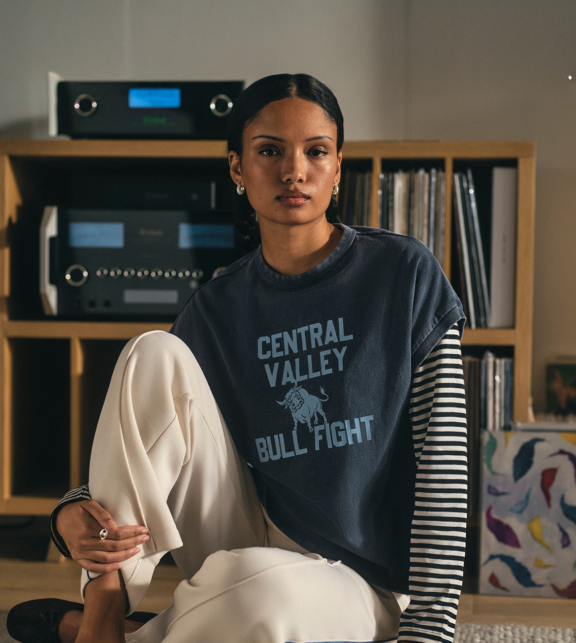 Person wearing a navy blue sweatshirt with 'Central Valley Bull Fight' text, sitting in a room with a bookshelf.