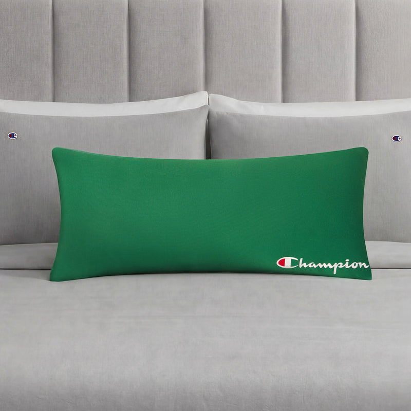 A green Champion Jersey Body Pillow, adding an athletic touch, rests on a neatly made bed with gray sheets and matching Champion-branded pillowcases, all set against a gray upholstered headboard.