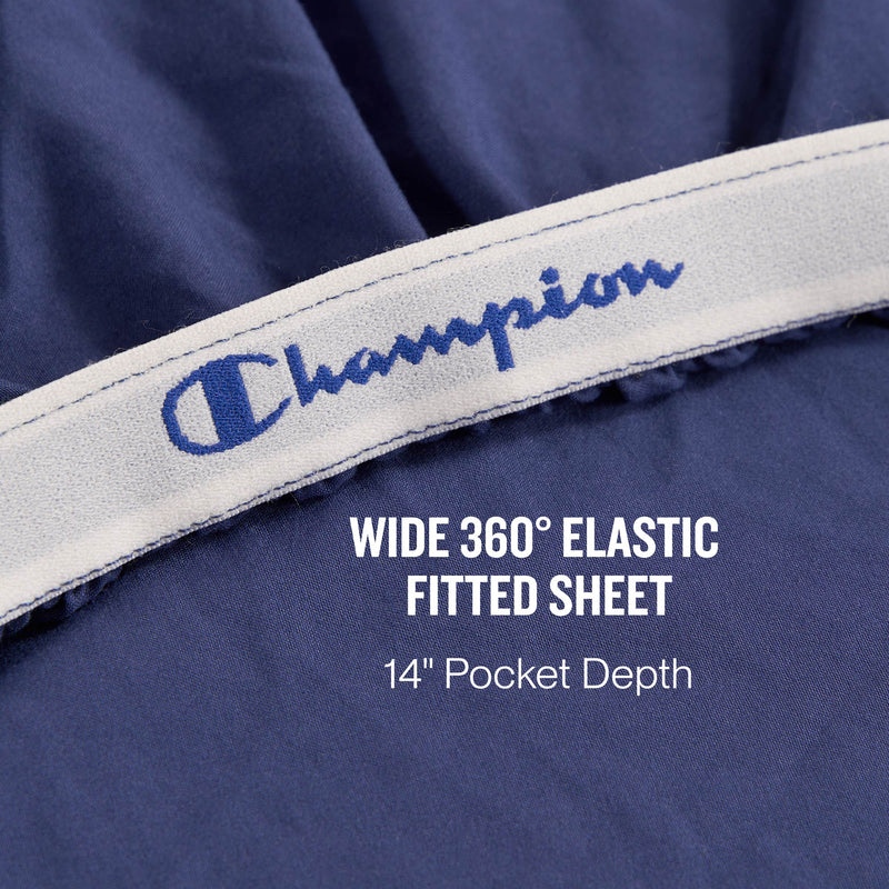 Close-up of the Peak Comfort Microfiber Sheet Set by Champion in navy blue, showcasing a wide 360-degree elastic band with text reading WIDE 360° ELASTIC FITTED SHEET, 14″ Pocket Depth—perfect for anyone looking for deep pocket sheets and athletic bedding comfort.
