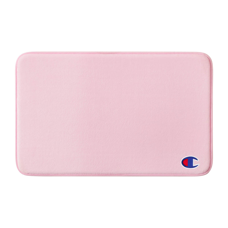 A rectangular, light pink Logo Patch Memory Foam Bath Mat by Champion, featuring rounded corners and a small red, white, and blue Champion logo patch at the bottom right corner. This skid-resistant bath mat combines style and safety for your bathroom.