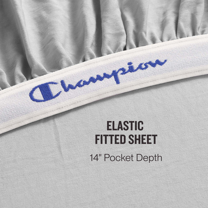 Close-up of a gray fitted sheet from the Champion Elastic Logo Microfiber Sheet Set, featuring an elastic band with the Champion logo. Text reads: Elastic Fitted Sheet, 14″ Pocket Depth—part of the premium Champion set.