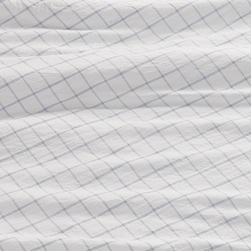 A close-up of a white fabric with a blue grid pattern, slightly wrinkled and textured, shows intersecting thin blue lines—these Champion Printed Microfiber Sheet Sets deliver both everyday comfort and stylish printed design.