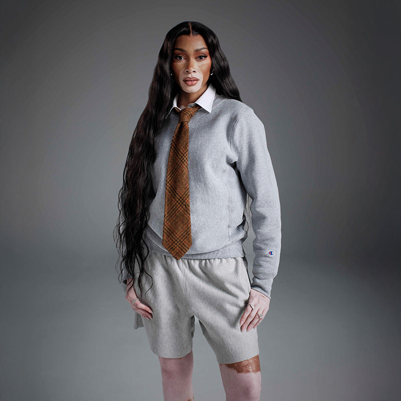 Person wearing a gray sweater, white shirt, and patterned tie with gray shorts against a gray background