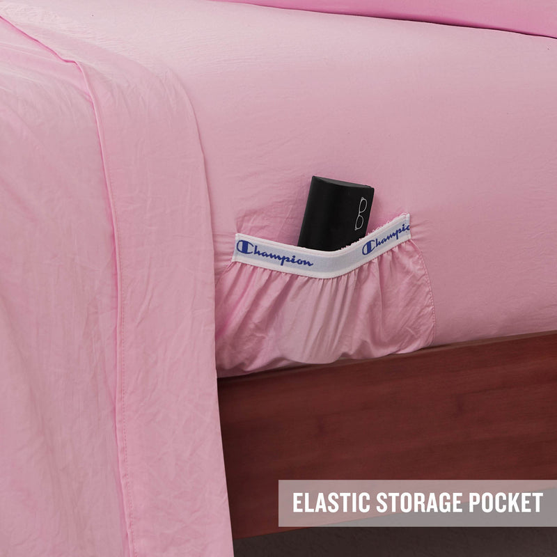 A pink Peak Comfort Microfiber Sheet Set from Champion features a convenient elastic storage pocket on the side, shown holding a black item that could be a glasses case. Designed with practicality in mind, this athletic bedding highlights the ELASTIC STORAGE POCKET text in the bottom right corner.