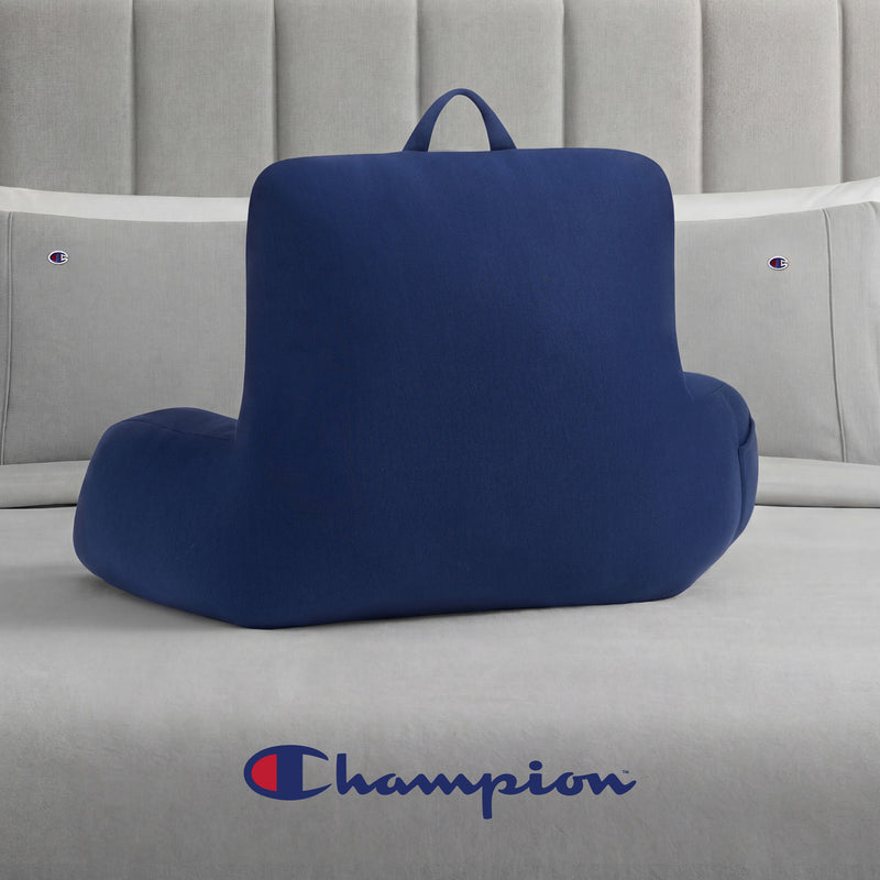 A Champion Jersey Backrest Pillow with supportive armrests and the iconic logo sits on a bed with gray bedding, which also features the Champion emblem.