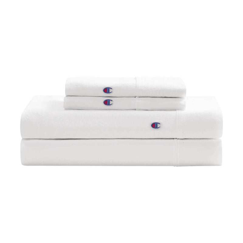 A neatly folded Embroidery Patch Microfiber Sheet Set by Champion, including two pillowcases and two sheets, each accented with a small blue and red embroidered Champion patch for an athletic-inspired bedding look.