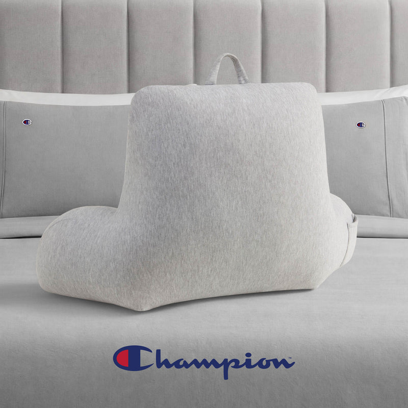 A Champion Jersey Backrest Pillow in light gray with armrests sits on a bed dressed in cozy gray jersey knit bedding. The Champion logo is featured on both the pillowcases and at the foot of the bed, bringing a signature Champion style to the room.